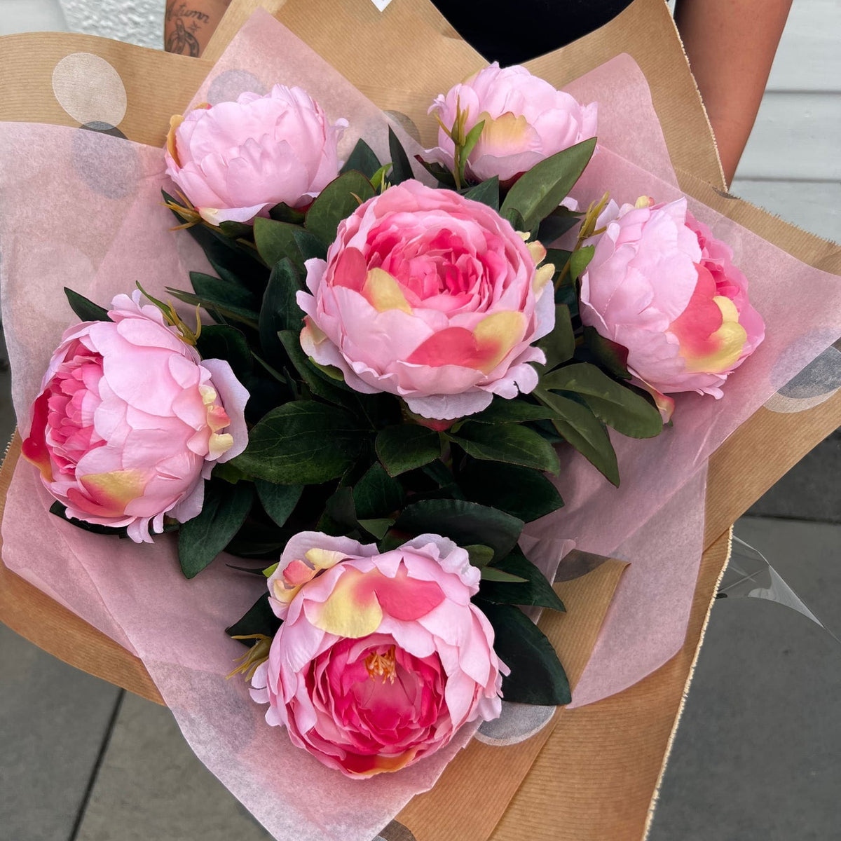 Pretty Pink Peony artificial bouquet wrapped in pink and kraft paper and held outdoors