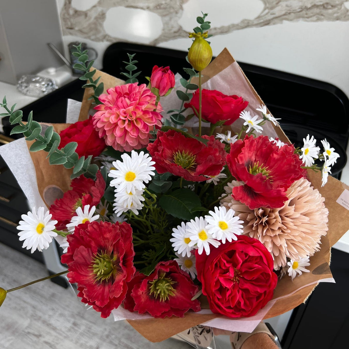 Simply Red artificial bouquet with crimson flowers and white daisies held in its presentation wrapping